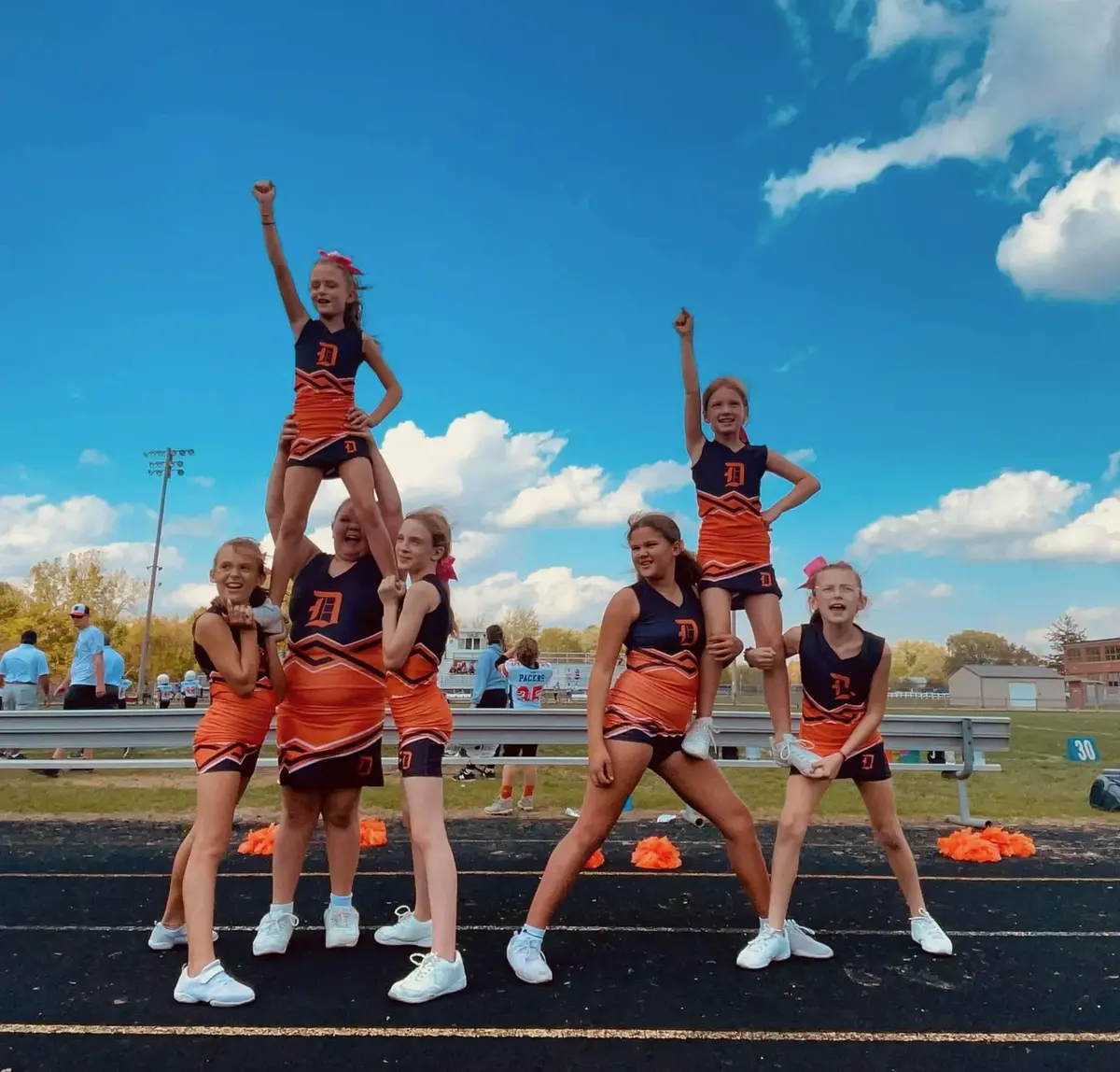 Jr Pacers cheer squad performing a pyramid stunt against a blue sky